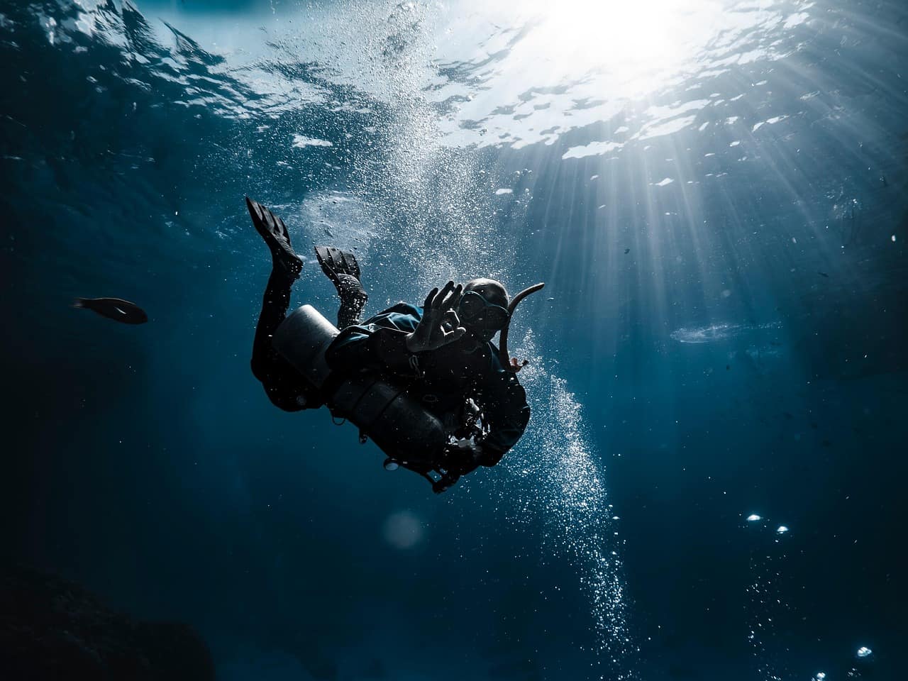 A diver suspended in turquoise water with shafts of Arabian Sea light cutting down from above